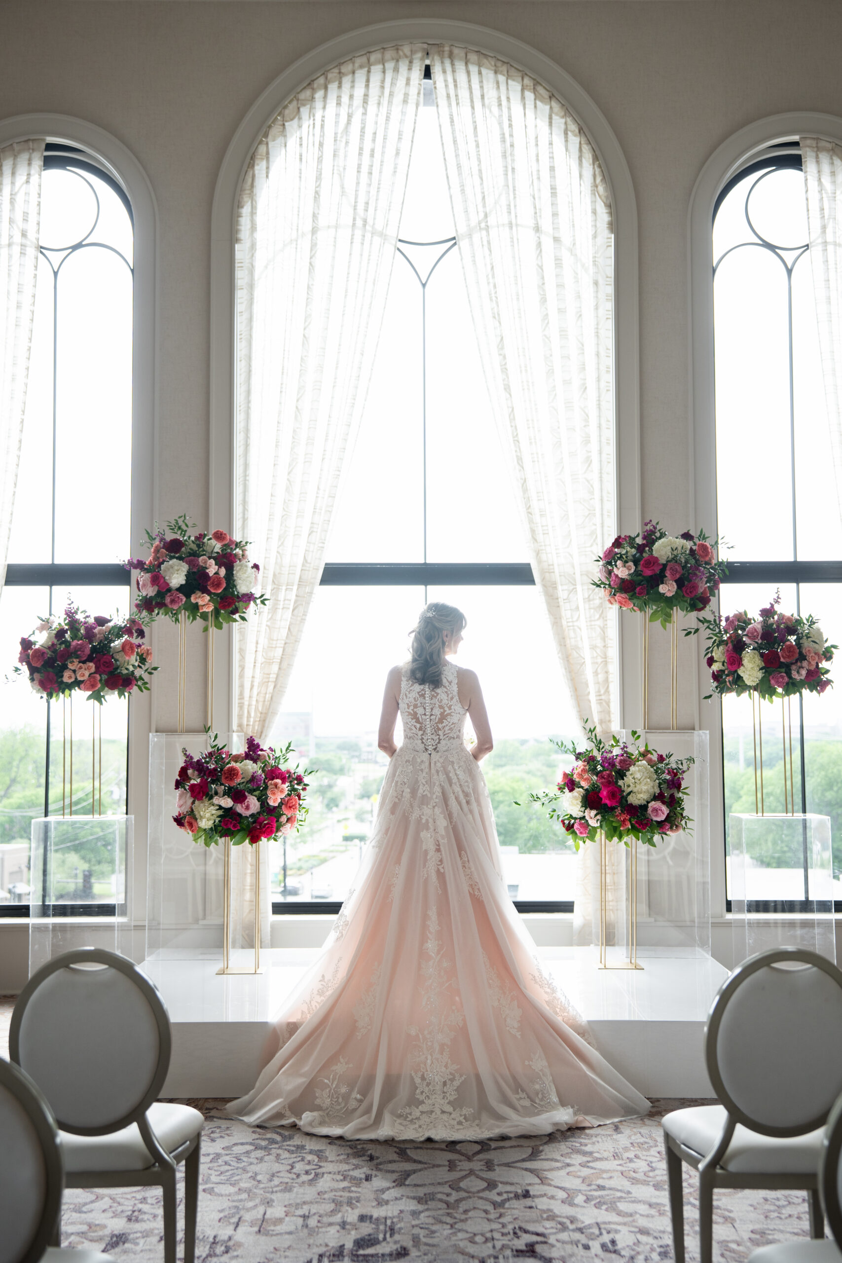 Bride standing in an elegant indoor wedding ceremony setting with floral arrangements